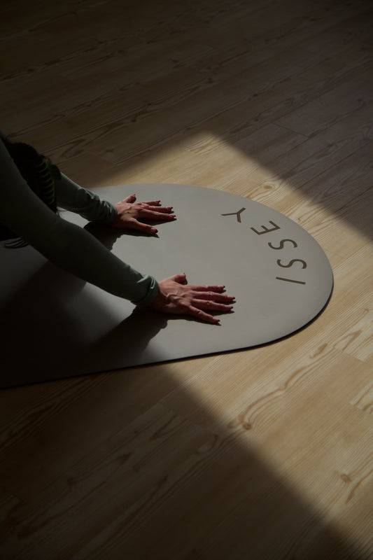 A person on a beige eco yoga mat with the brand name 'ISSEY' printed on it, in a downward facing dog.